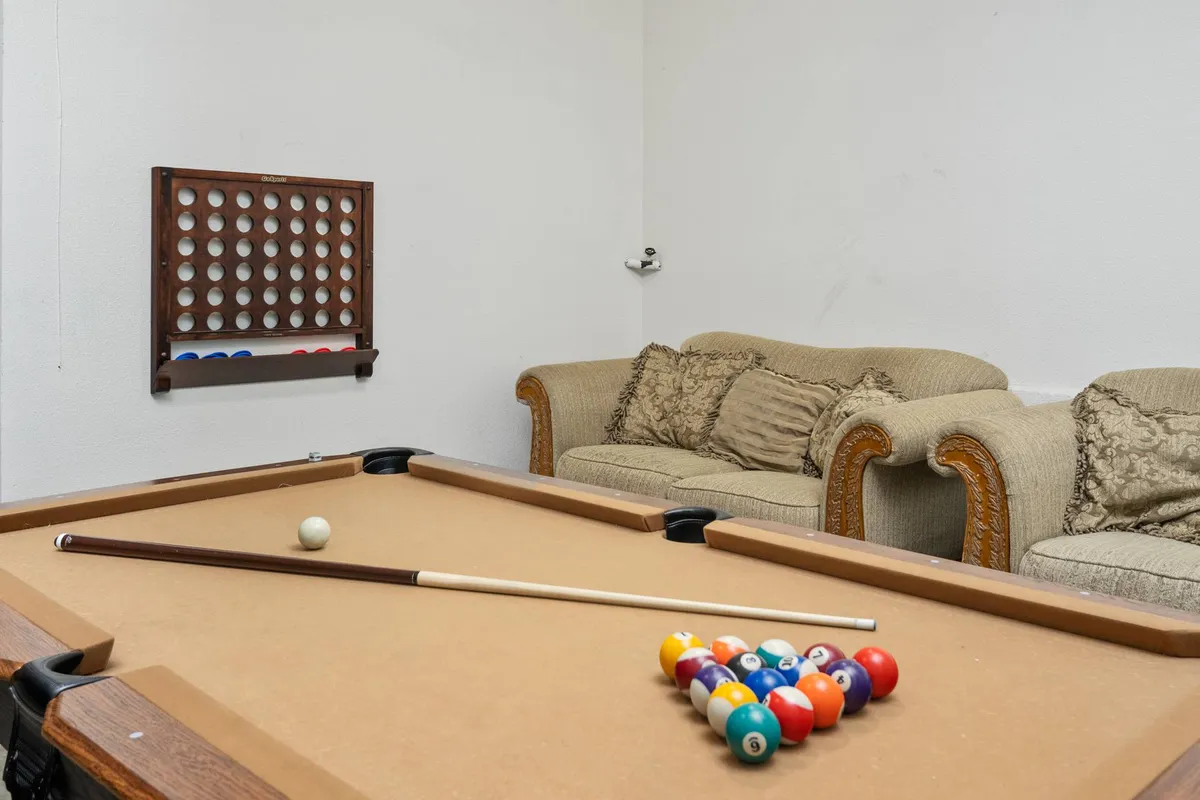 A playful and relaxed interior featuring a pool table, a cozy couch, and game-inspired wall art. The setting is designed for casual fun, family tournaments, and memorable celebrations.