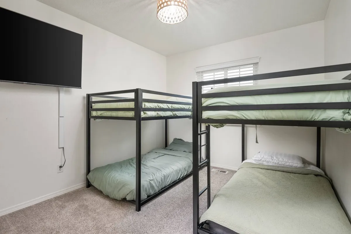 A bright and welcoming bunk room with twin-over-twin bunk beds, a television, and natural light pouring in through the window. The space is playful yet comfortable, ideal for children or group sleepovers.