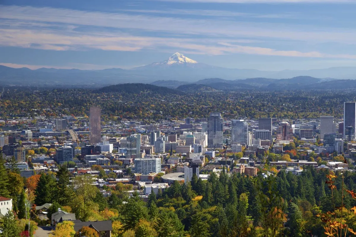 A scenic view capturing Mount Hood in the distance, the downtown skyline, and vibrant fall foliage. The image evokes the feeling of adventure, with opportunities for hiking, sightseeing, and nature walks nearby.