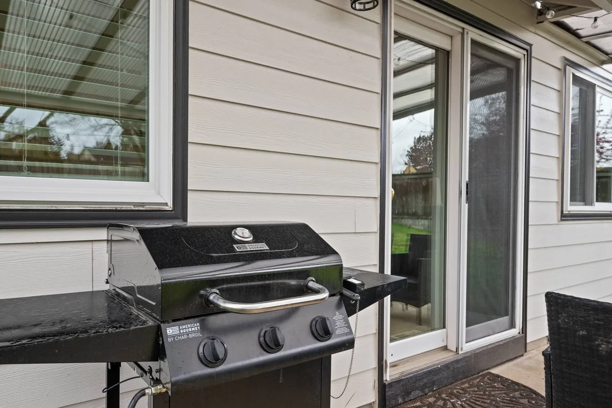 An inviting backyard patio featuring a grill and sliding door, with space for outdoor entertaining, barbecuing, and relaxing with friends. The area is set up for gatherings and social activities, ideal for enjoying warm evenings after a day out.