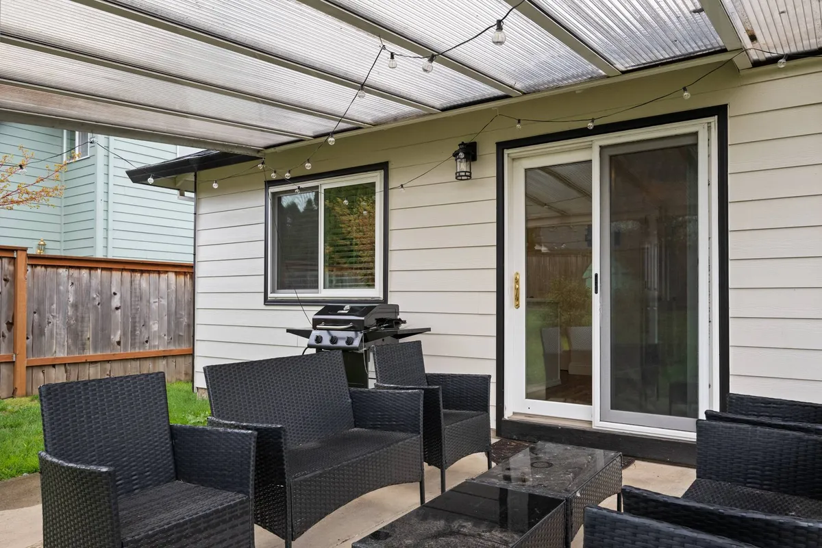 This image highlights a relaxing backyard setting featuring a comfortable outdoor seating area, a BBQ grill, and a sliding glass door leading indoors. The space is inviting, perfect for gatherings, and offers ample room for both adults and pets to enjoy the outdoors together.
