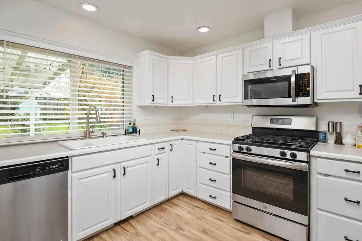 The kitchen shines with stainless steel appliances, white cabinetry, and a kitchen sink overlooking a window. Ample counter space sets the stage for culinary creativity, from baking cookies to preparing family dinners, while an abundance of natural light reinforces the inviting atmosphere.