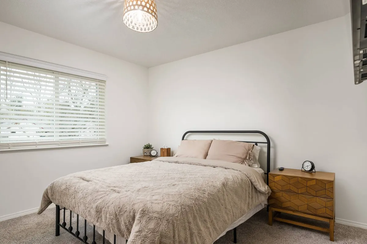 A sunlit queen bedroom featuring a plush bed with soft bedding, flanked by wooden nightstands and illuminated by a unique light fixture. The room exudes warmth, comfort, and tranquility, making it perfect for rest and relaxation.