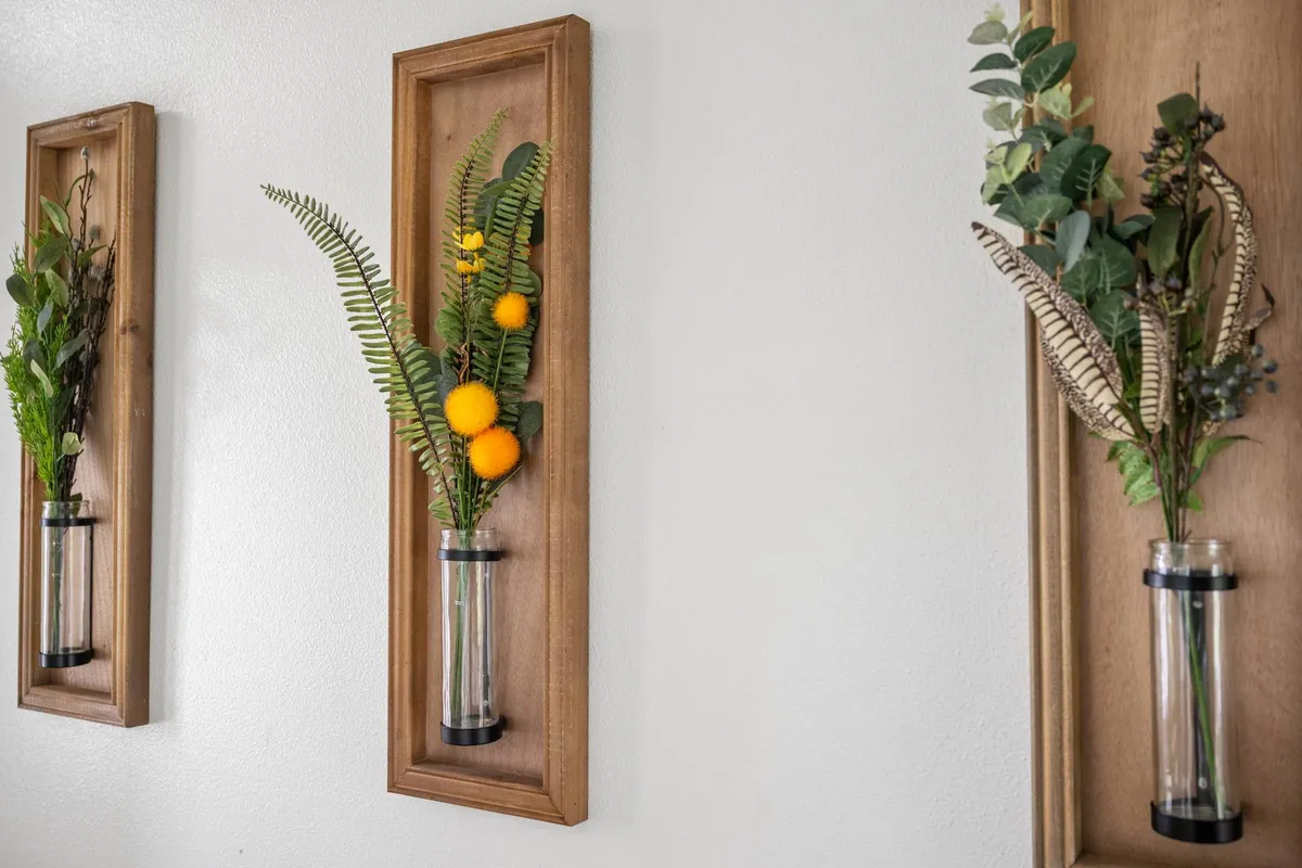 This image showcases a tranquil corner adorned with wall-mounted vases filled with greenery and yellow flowers, emphasizing a connection to nature even while indoors. People are seen admiring the art and engaging in conversation, contributing to a warm and welcoming environment.