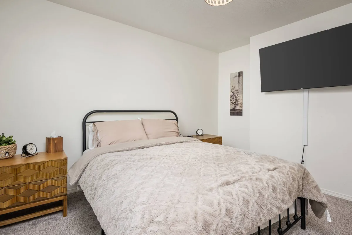 A cozy bedroom scene featuring a plush bed, matching nightstands, decorative wall art, and a television. The space is softly lit, exuding warmth and inviting relaxation, perfect for restful evenings or slow mornings.
