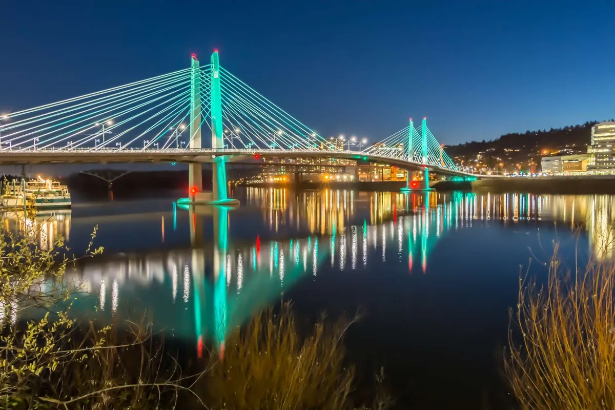 An inviting exterior scene featuring a bridge over water, with city lights reflecting on the surface and a tranquil ambiance that encourages evening gatherings or strolls near the water's edge.